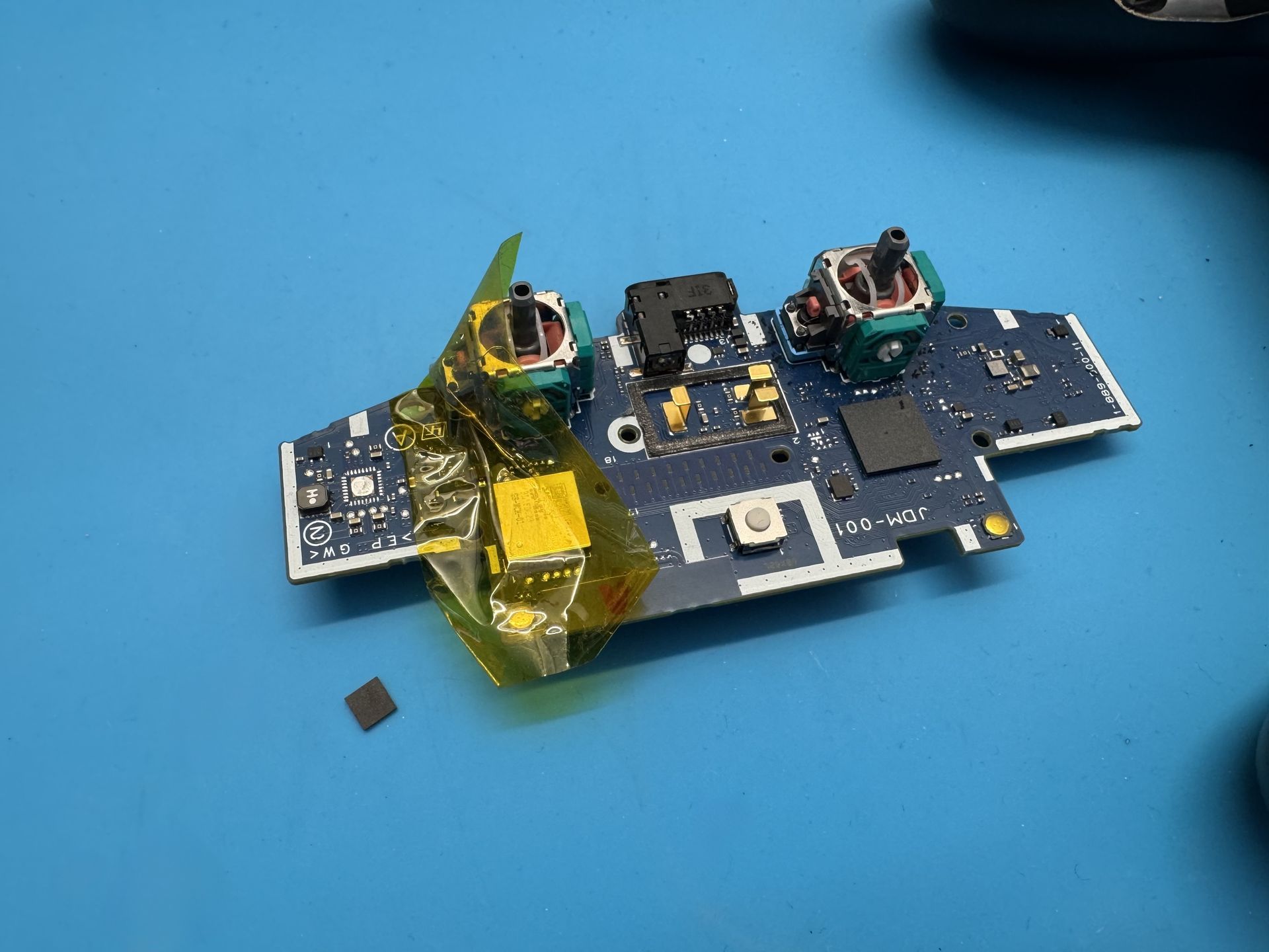 motherboard from a PS4 controller placed on a pad with a desoldered microchip